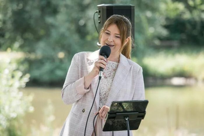 Annika Schmitz singt mit Mikrofon bei einer Trauung im Grünen